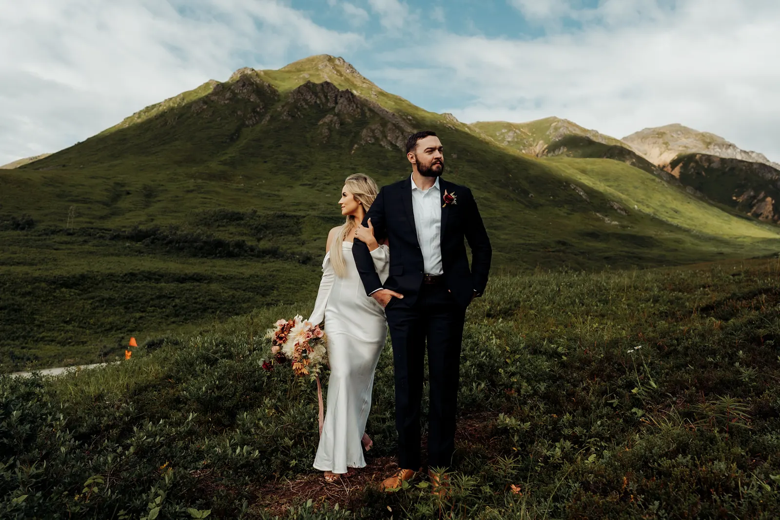A bride and groom standing together in a green mountain valley.